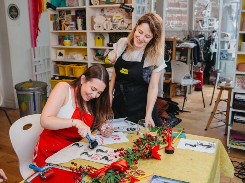 Woman pressing stamp onto paper with art teacher watching